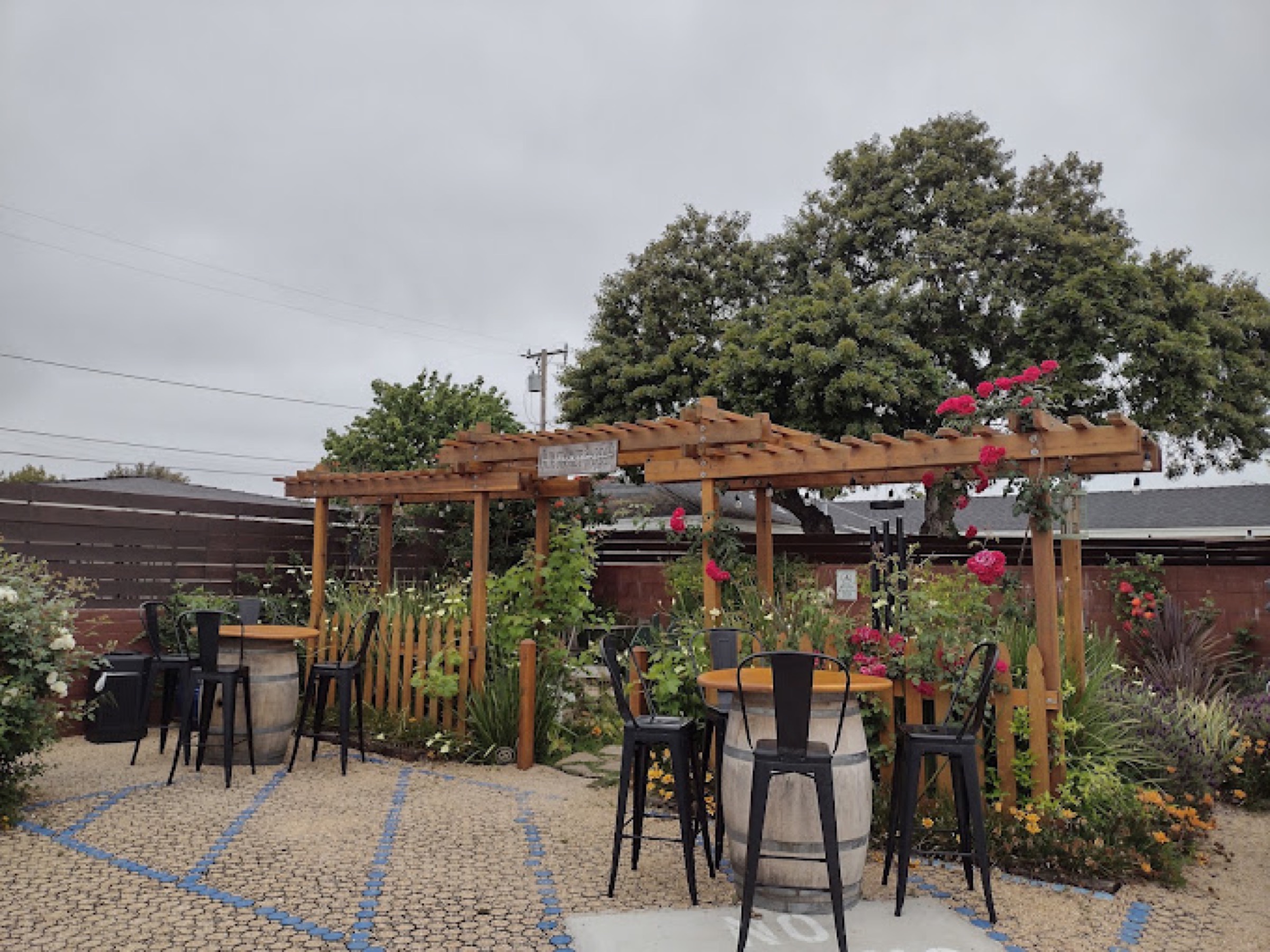 Crocker's garden patio under a wood pergola with climbing roses and wine-barrel tables